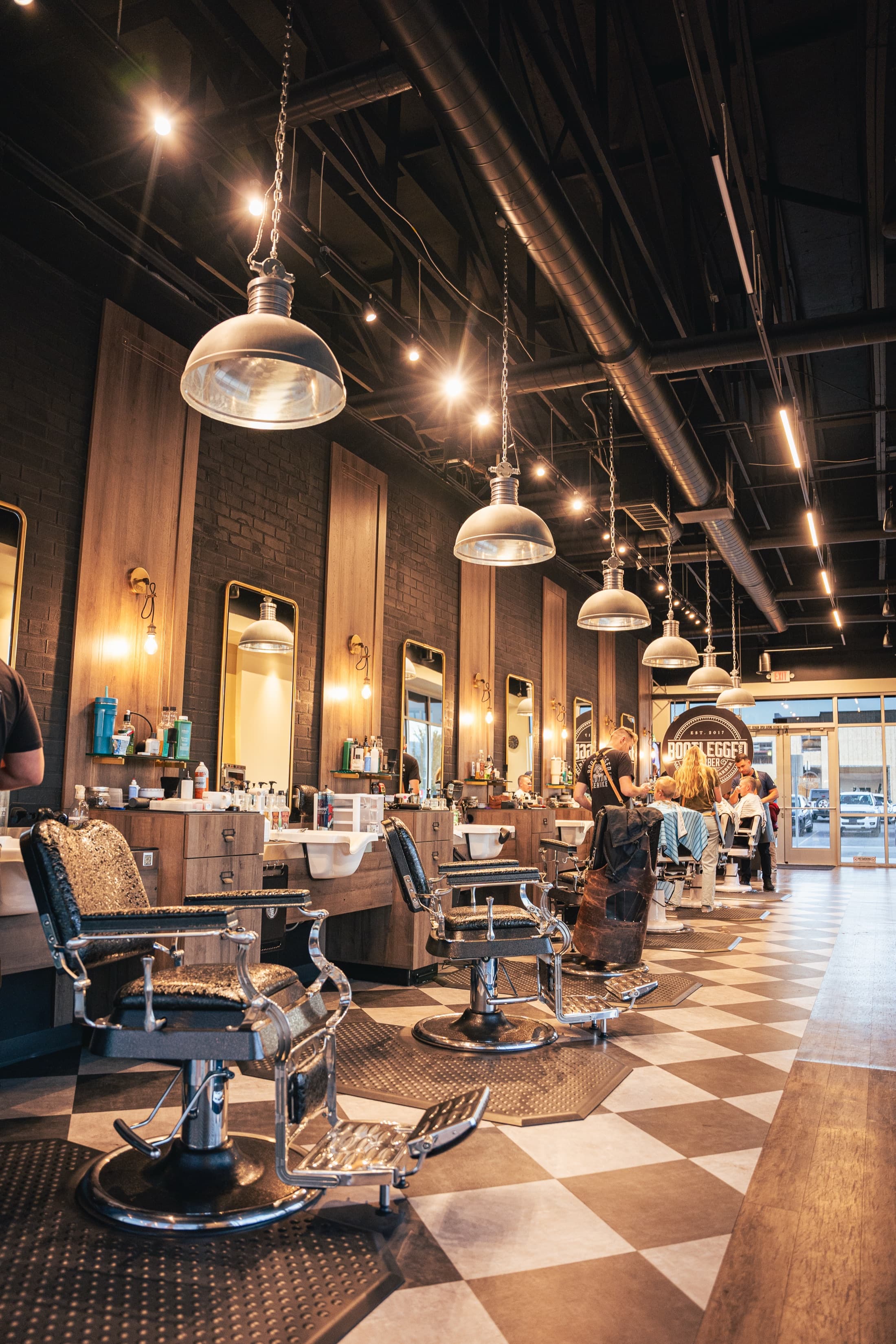 Row of vintage black-and-chrome barber chairs under industrial pendant lamps at Bootlegged Barber Herriman
