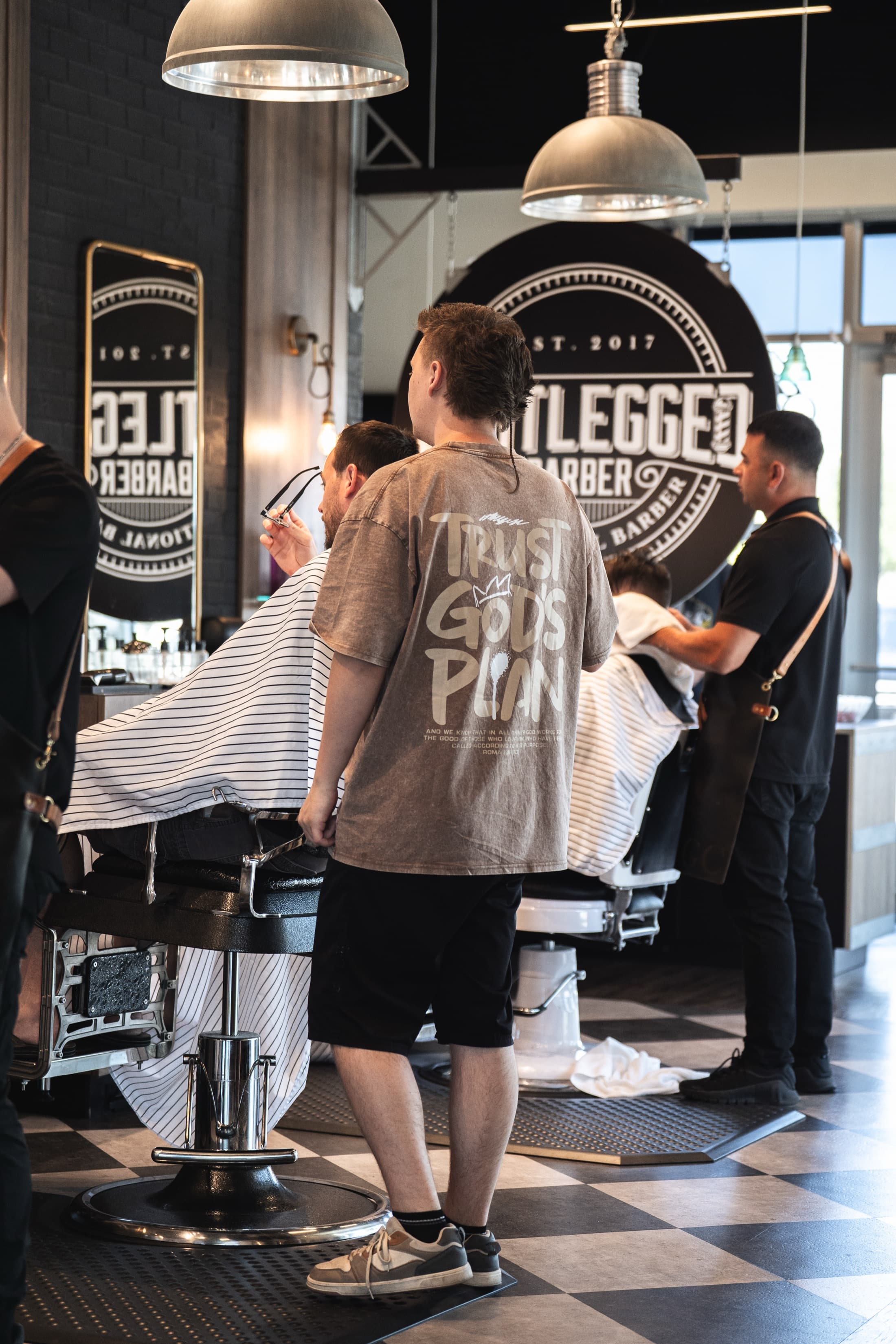 Barbers working caped clients in vintage chairs down the Bootlegged shop floor